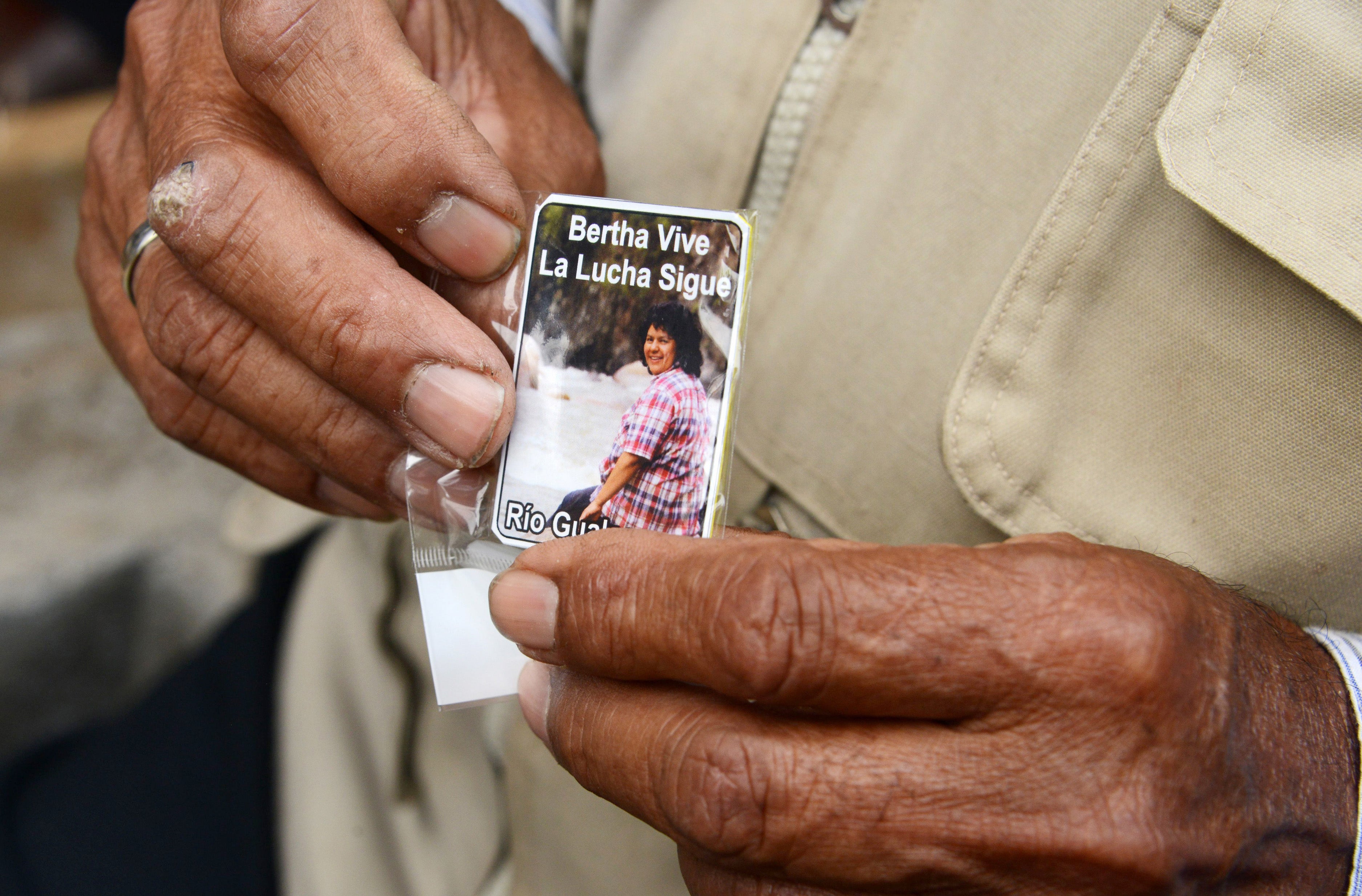 man holds a card bearing a picture of Cáceres, which reads ‘The fight continues’