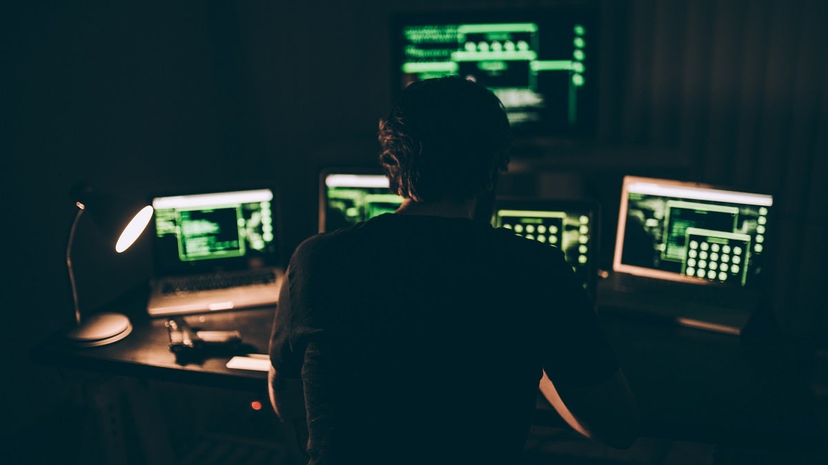 Man sitting in dark room surrounded by computer monitors