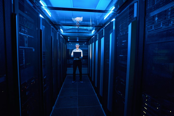 Server Administrator Standing In Hallway Of Data Center