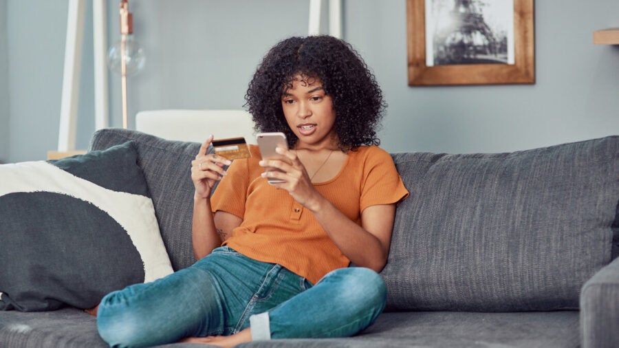 Young woman sitting on the couch doing some shopping on her mobile device