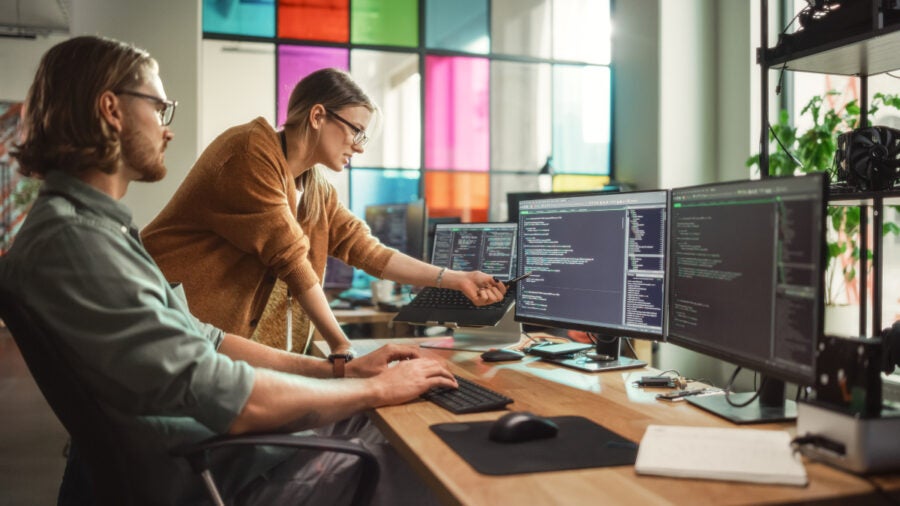 Male Programmer Shows Progress To Female Start Up Ceo On Desktop Computer In Creative Office Space. Caucasian Man And Woman Discussing New Features For Artificial Inteligence Software.