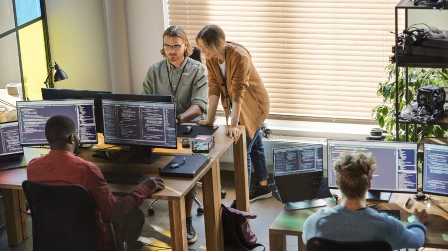 Creative Office: Diverse Colleagues Coding On Desktop Computers With Multiple Monitors. Female Project Manager Talks To Male Team Lead While Junior Developers Working On Mobile Application.