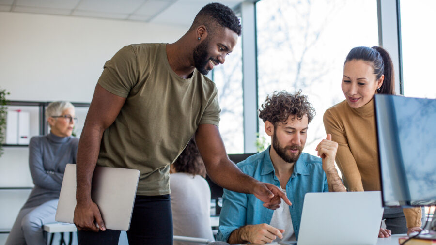A Team Of Creative Professionals Looking At The Lap Top And Brainstorming Ideas.
