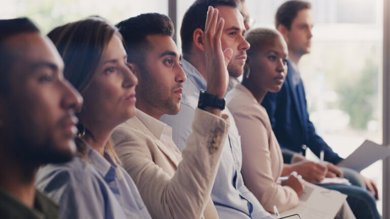 Shot Of A Young Businessman Raising His Hand During A Conference In An Office